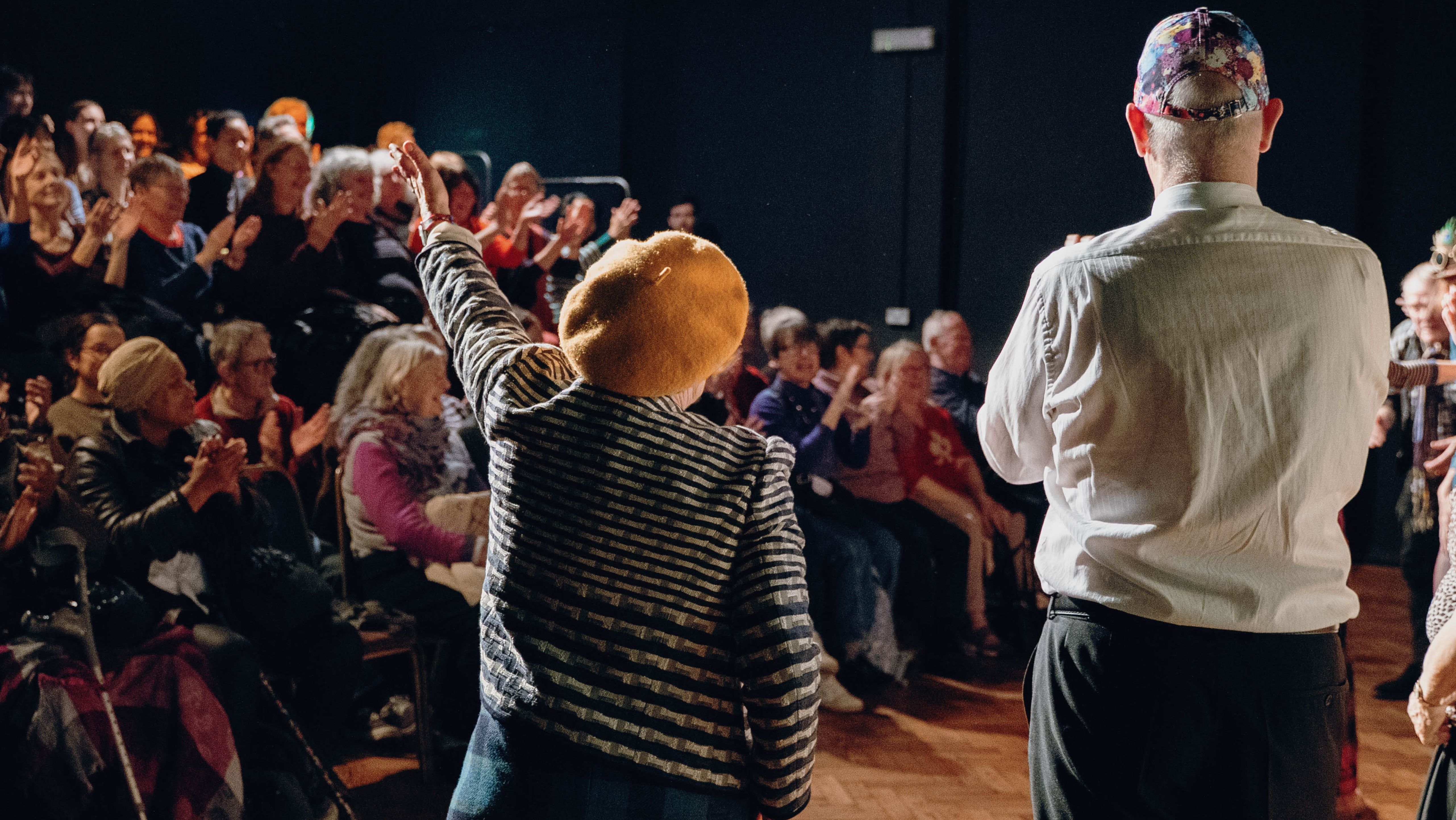 Reclaim The Street Performance Image of a man on a woman from behind. The woman has one hand extended, as if she just blew a kiss to the audience, visible in front of her.