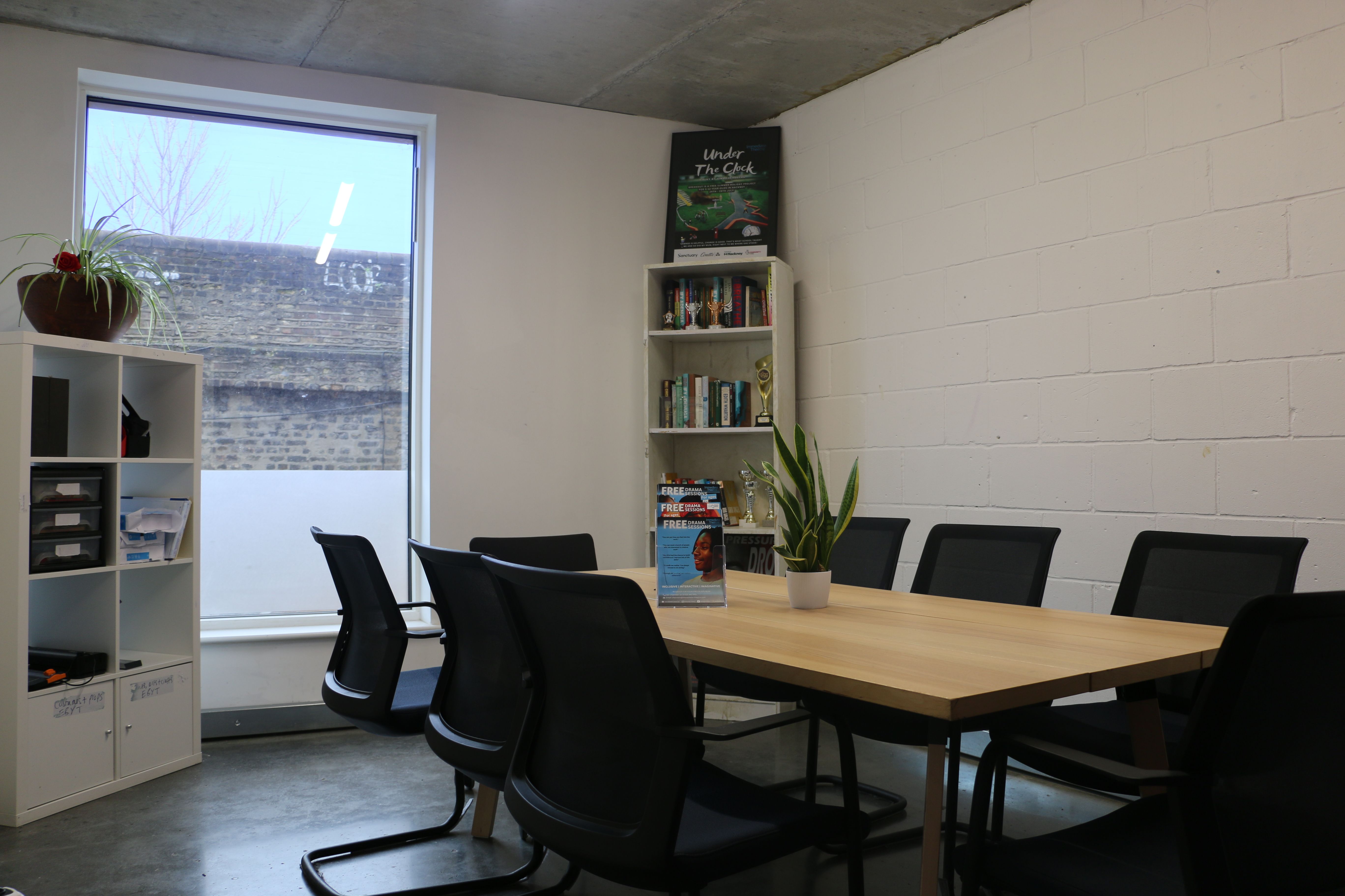 Meeting Room Room with a large table in the the middle. There are several chairs around the table and a large window at the rear of the room flagged by two book shelves on either side